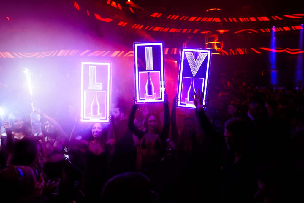 Servers holding bottle presentation LED signs that spell out "LIV".