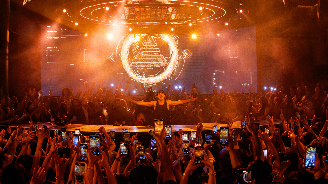 Crowd angle facing John Summit with his arms stretched out looking and smiling into the crowd with his logo behind him on the LED screen