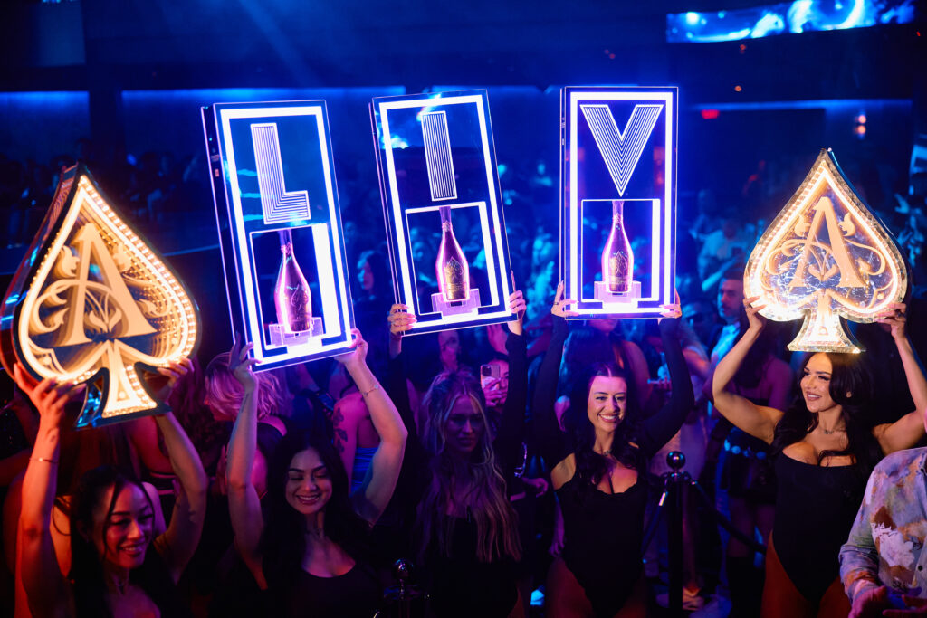 Bottle servers holding neon letters spelling out "LIV" and Perrier Jouët signs