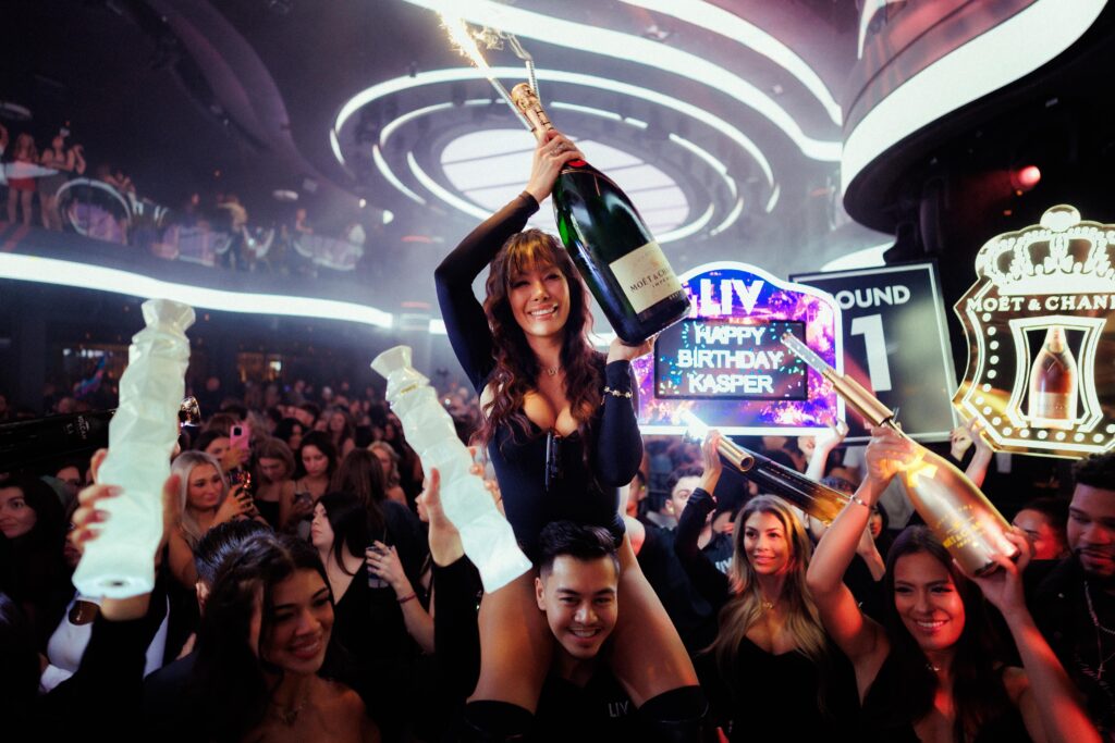 Server holding a champagne bottle presentation in the air and smiling.