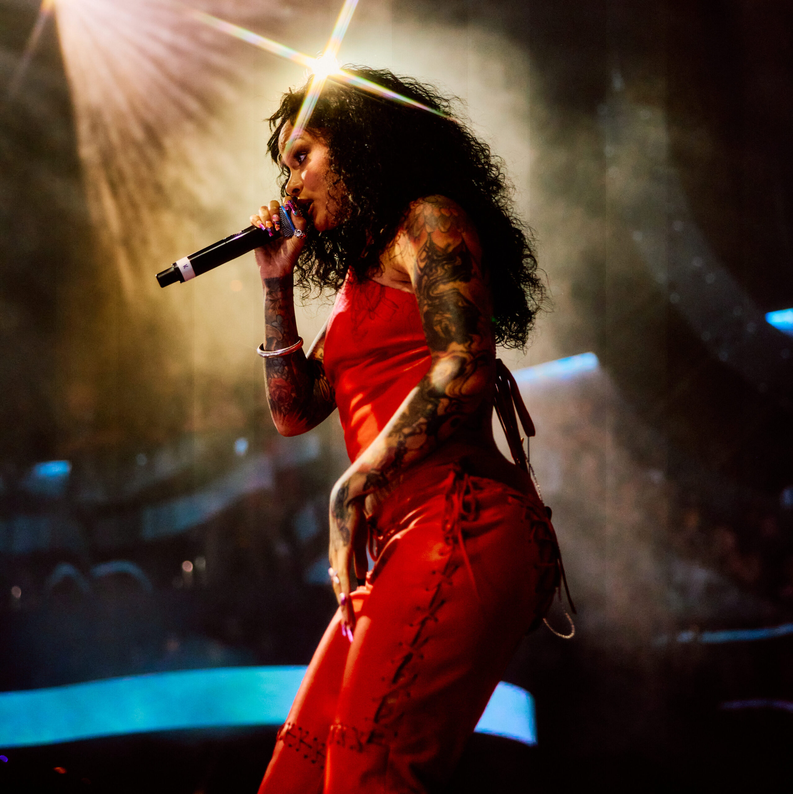 Kehlani from a side angle, singing into her microphone towards the crowd.