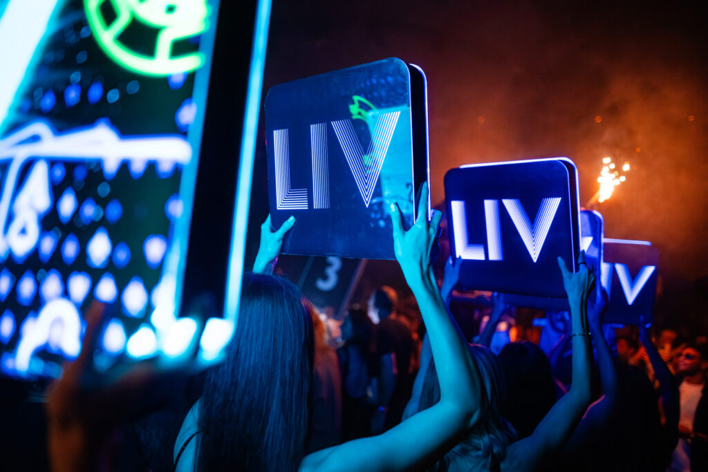 Bottle servers in line and holding up neon signs that read "LIV".