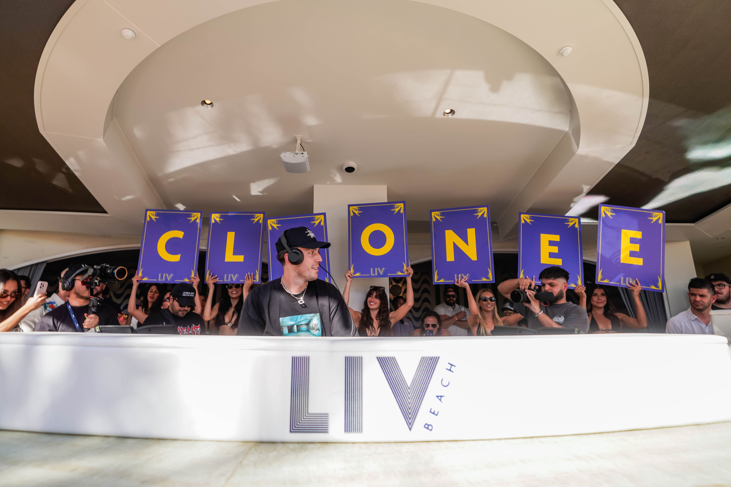 Cloonee behind the DJ Booth looking sideways and in front of letterboard signs that spell out "Cloonee".