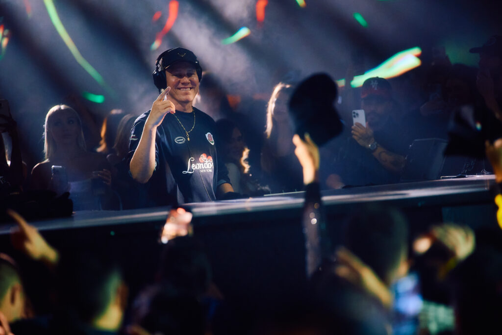 Tiësto smiling behind DJ booth performing at LIV nightclub with crowd and colorful lights.