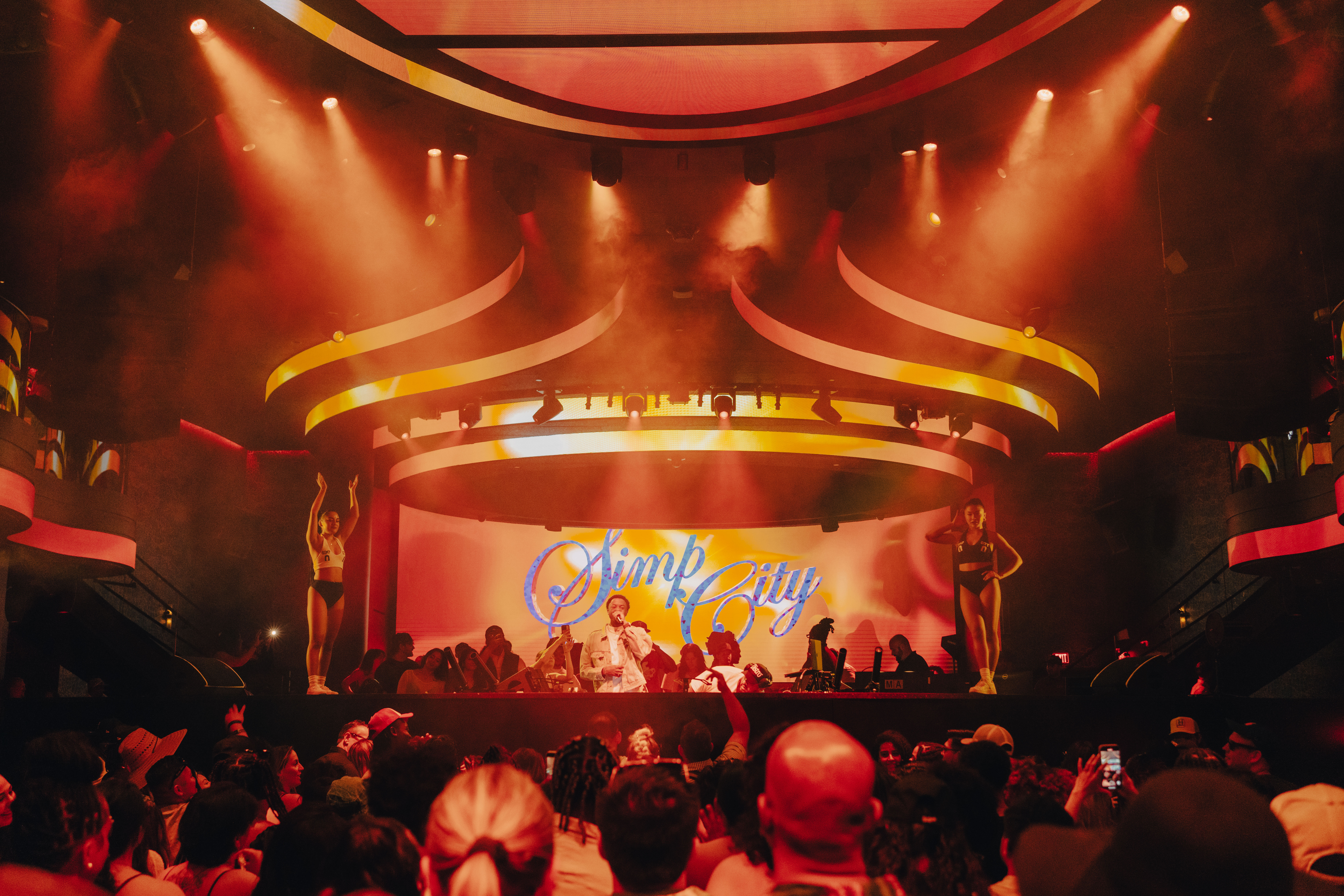 DJ behind the booth with "Simp City" displayed behind him on the LED.