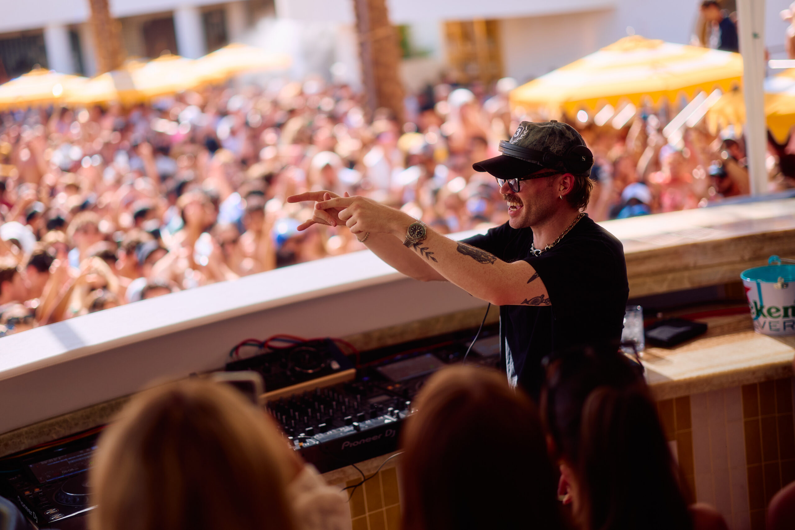Dom Dolla behind at LIV Beach DJ booth with arms raised as a packed crowd dances and cheers behind him.