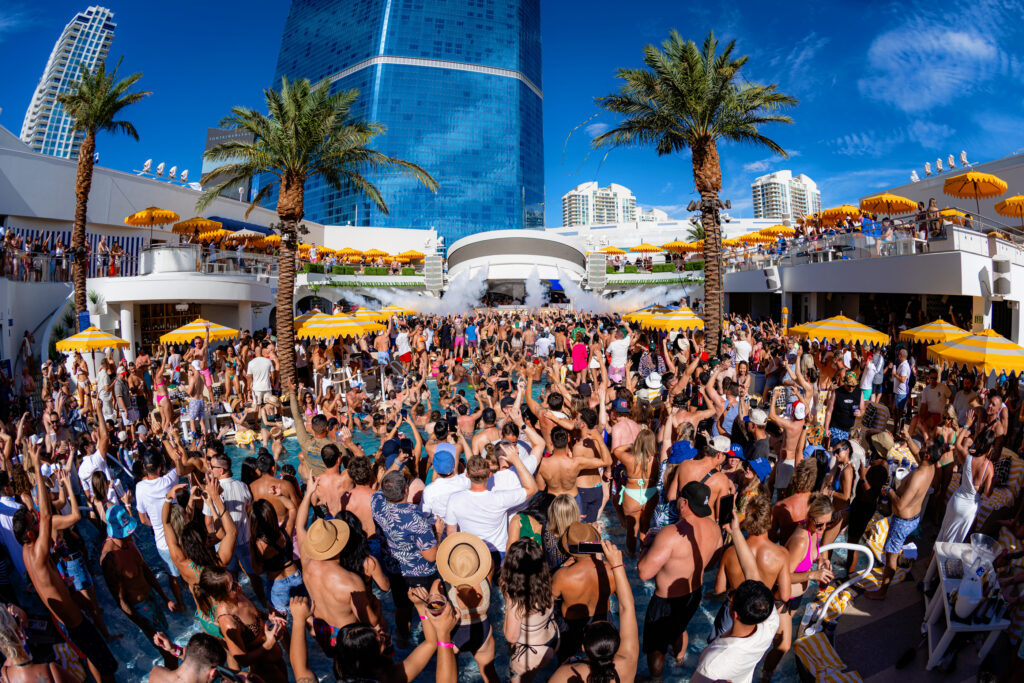 Packed LIV Beach dayclub crowd celebrating poolside with palm trees and high-energy atmosphere.
