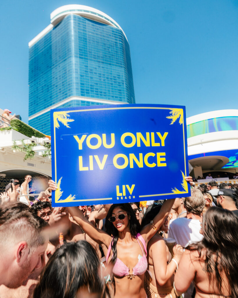 Model cocktail server holding a presentation sign which reads, "You Only LIV Once".