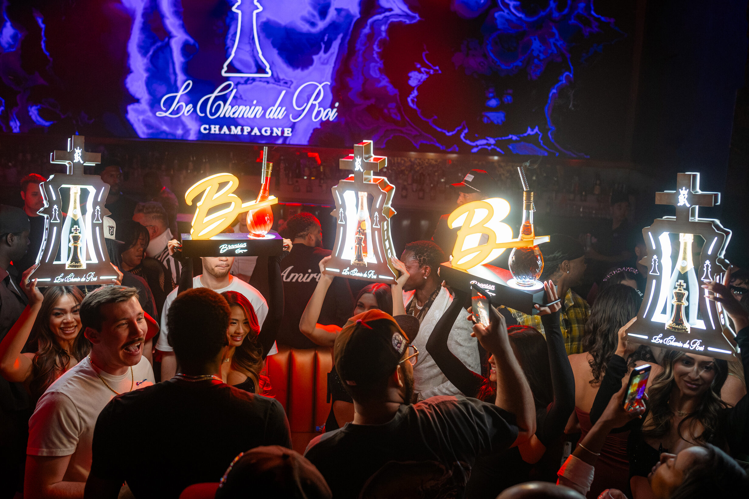 Model cocktail servers holding bottle presentation signs that display the Branson Cognac logo.